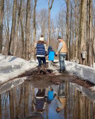 Family with son enjoying playing in fresh snow during wintertime and walking through melting puddles