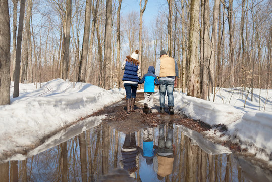 Family with son enjoying playing in fresh snow during wintertime and walking through melting puddles