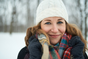 Confident blong woman sanding outside in the snow and fighting the cold with a plaid wool scarf