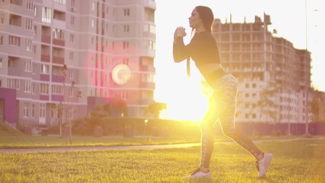 young fit and energetic woman doing sport workout and fitness lunge exercises with weights for healthy lifestyle in city park during sunset.