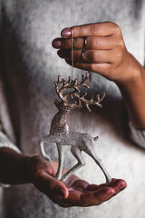 Woman in sweater holding toy deer glass decorative ball in hands, copy space. Christmas, new year