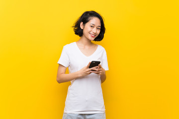 Asian young woman over isolated yellow wall sending a message with the mobile