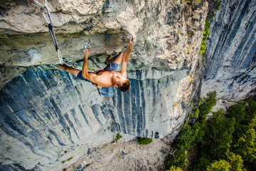 Shirtless fit man hanging on one finger high up under a roof of rock