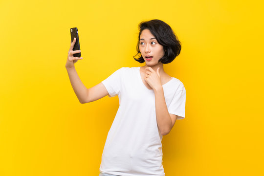 Asian young woman over isolated yellow wall making a selfie