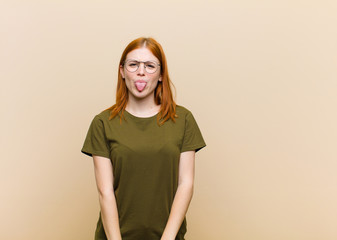 young red head pretty woman feeling disgusted and irritated, sticking tongue out, disliking...