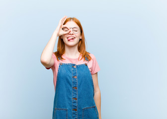 young red head pretty woman smiling happily with funny face, joking and looking through peephole,...