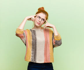 young pretty red head woman looking concentrated and thinking hard on an idea, imagining a solution...