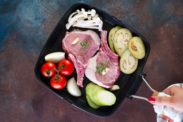 hand holds grill pan with Raw lamb ribs marinating with buna-shimeji and tomato on stone background , flat lay