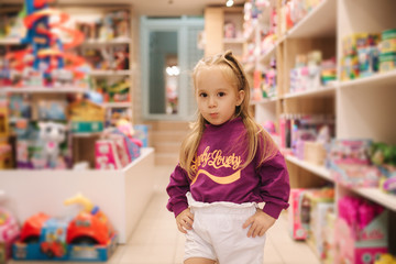 Adorable little girl shopping for toys. Cute female in toy store. Happy young girl selecting toy