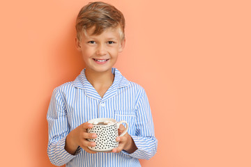 Cute little boy drinking hot chocolate on color background
