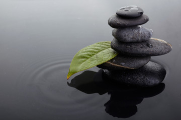 Zen stones in balanced pile and green leaf with water drops in water
