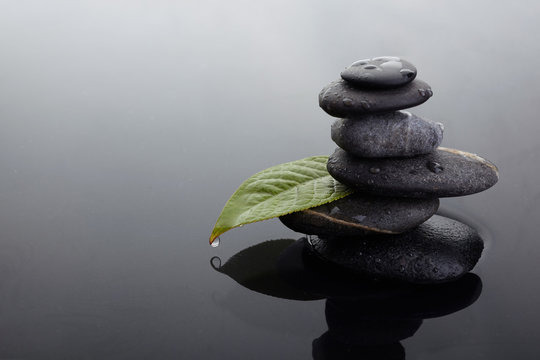 Zen stones in balanced pile and green leaf with water drops in water