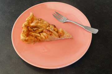 Piece of apple tart and fork on a red plate