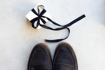 Gift box with black ribbon, man's shoes on white background. Lovely gift special for the best dad or grandfather. Father's day or birthday. Congratulation concept.