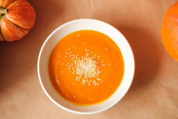 homemade fresh sweet pumpkin soup with sesame seeds in a plate on a table with pumpkins. Thanksgiving, vegetarian concept