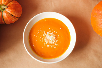 homemade fresh sweet pumpkin soup with sesame seeds in a plate on a table with pumpkins. Thanksgiving, vegetarian concept