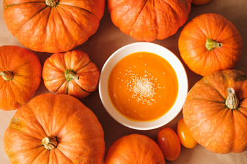 homemade fresh sweet pumpkin soup with sesame seeds in a plate on a table with pumpkins. Thanksgiving, vegetarian concept