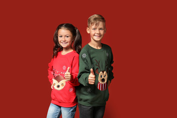 Cute children in Christmas sweaters showing thumb-up on color background