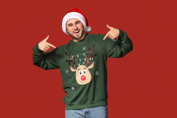 Young man in Christmas sweater and Santa hat on color background