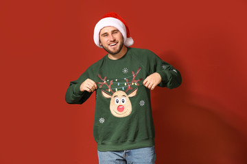 Young man in Christmas sweater and Santa hat on color background