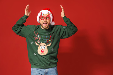 Funny man in Christmas sweater and Santa hat on color background