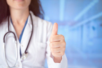 Young handsome doctor woman wearing stethoscope over hospital background approving doing positive gesture with hand, thumbs up smiling and happy for success. Winner gesture.