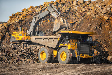 Open pit mine industry, excavator loading coal on big yellow mining truck for anthracite