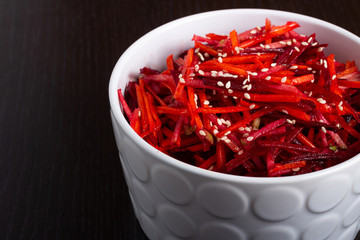 Vegetable salad of apple, carrot and beetroot with lemon juice, sesame seeds and vegetable oil in a white deep plate