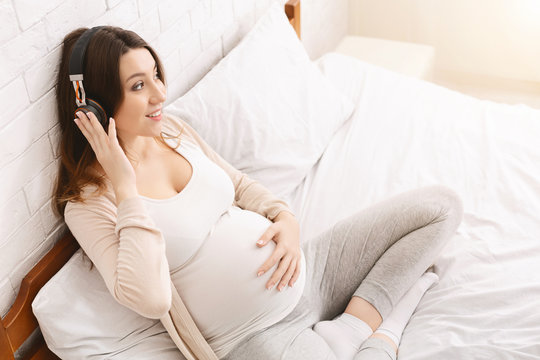 Tranquil pregnant woman listening to music with wireless headphones