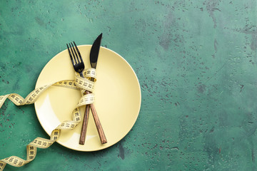 Cutlery with plate and measuring tape on color background. Concept of diet