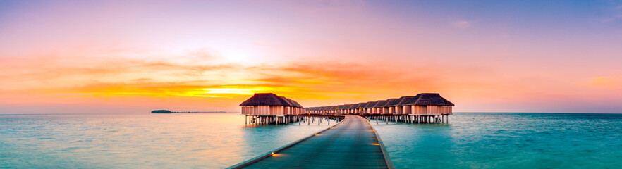 Amazing sunset panorama at Maldives. Luxury resort villas seascape with soft led lights under colorful sky. Beautiful twilight sky and colorful clouds. Beautiful beach background for vacation holiday