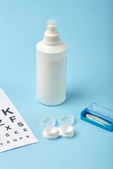 Flat composition with contact lenses, table for eye examination. Accessories for ophthalmologists. Glasses and lenses for vision correction on a blue background