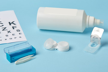 Flat composition with contact lenses, table for eye examination. Accessories for ophthalmologists. Glasses and lenses for vision correction on a blue background