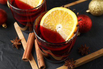 Glasses of tasty mulled wine and christmas baubles on black background, close up