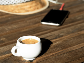 Fragrant espresso coffee on a wooden table. In the background is a straw hat and a telephone. Close-up.