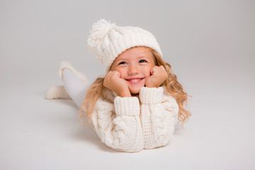 Winter clothes. Portrait of a little curly-haired girl in a knitted white winter hat. little blonde girl in white knitted hat and sweater smiling light background isolate, space for text