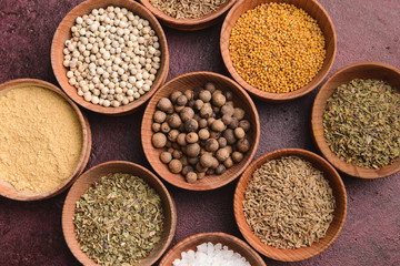 Bowls with different dry herbs and spices on color background