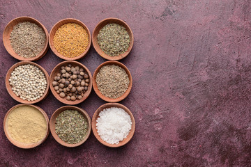 Bowls with different dry herbs and spices on color background