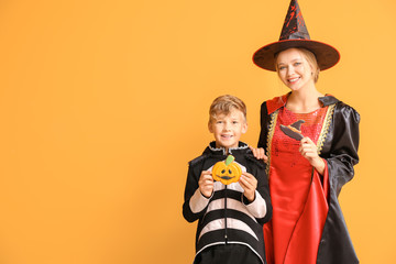 Mother with little son in Halloween costumes and with cookies on color background