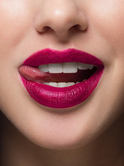 Fototapeta premium Close-up of sexy female lips with tongue. Clean skin and a clear lip contour are outlined with a fashionable marsala lipstick. White teeth and the beauty of smile for stamotologii, spa or cosmetology