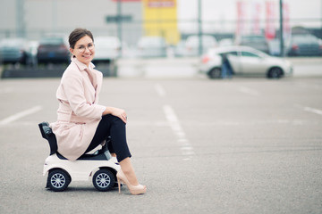 young woman sits on a children's plastic car
