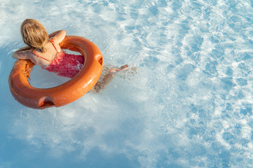 Young baby girl relaxing and swimming in the blue swimming pool with a orange circle closeup.