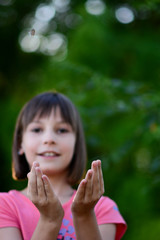 Fototapeta premium Little girl catching butterfly in the garden with her hands. Girl having fun in the garden catching successfully butterfly only with her hands.
