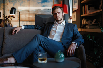 Young and charming businessman is thinking about business while sitting on the sofa in his modern...