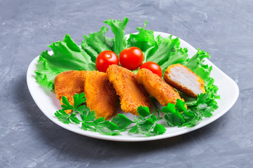 Set of delicious golden fried chicken nuggets with lettuce, parsley and three cherry tomatoes on a white plate