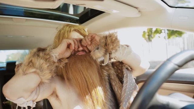 Somber caveman covered in hair driving modern car like professional. Portrait of savage wiping his eyes observing with surprise modern architecture cityscape.