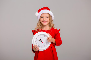 little blonde girl in Santa suit with white clock smiling on light background