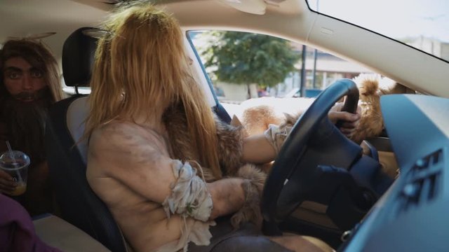 Archaic long-bearded caveman driving a modern car with leg on window. Prehistoric people traveling on car through city. Fun homo sapiens.