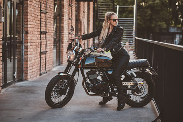 Fototapeta na wymiar Female biker in full leather suit is posing for photographer while sitting on her brand new motorbike.