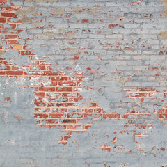 Gray paint is weathered and peeling off a red brick wall